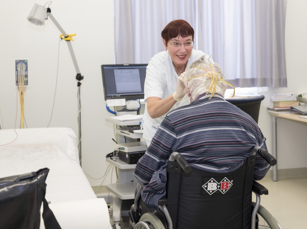 Ärztin behandelt älteren Patient im Rollstuhl auf der Neurologischen Ambulanz